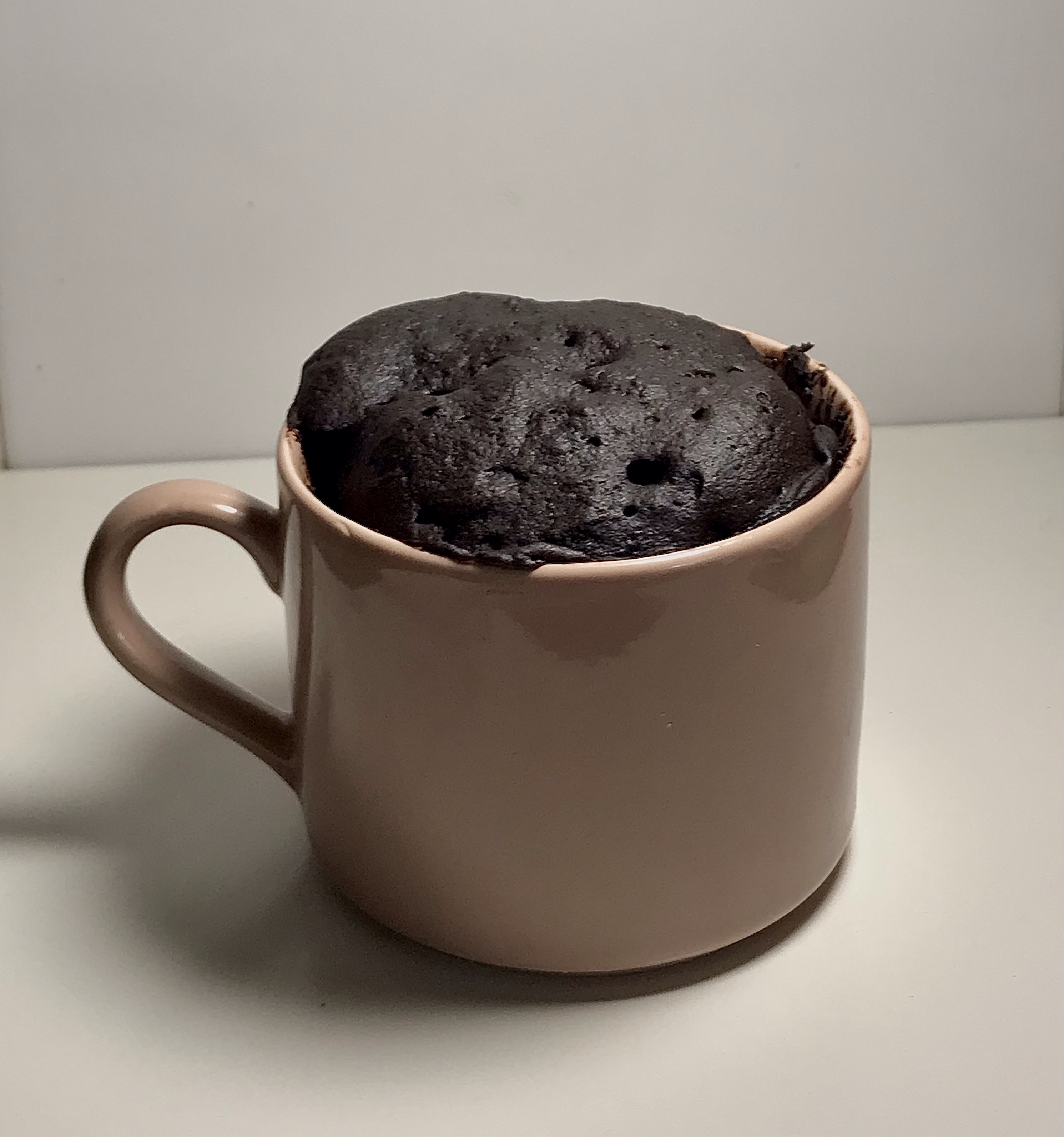 Chocolate cake in a pink ceramic mug on white countertop with white background